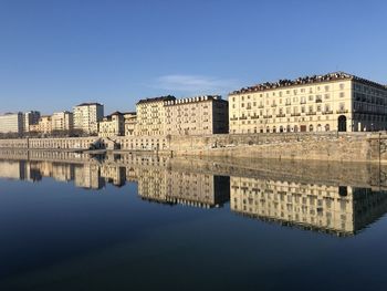 Reflection of buildings in lake against clear blue sky