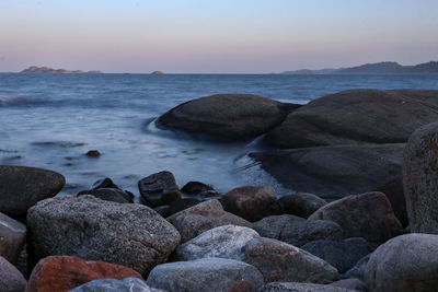 Rocks in sea against sky during sunset