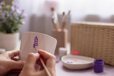 Female paints with a brush a sprig of a lavender flower, on a ceramic pot