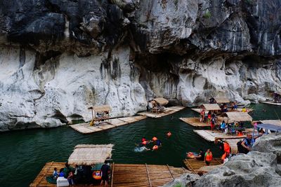 People on wooden rafts in lake against rock formation