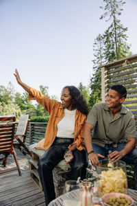 Young woman waving while sitting with male friend during party