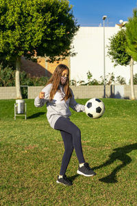 Full length of girl wearing mask playing soccer ball on grass