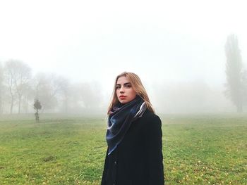 Portrait of woman standing on field in foggy weather