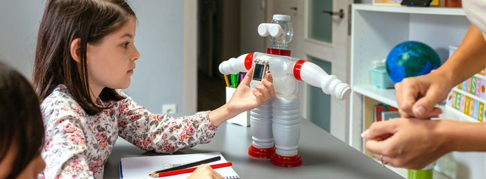 Female student holding solar panel over recycled toy robot in a robotics class