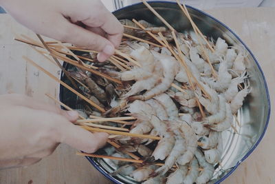 Close-up of hands holding shrimps with skewers in bucket