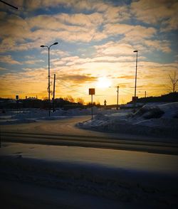 Snow covered road against sky during sunset