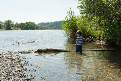 Boy standing by lake against trees