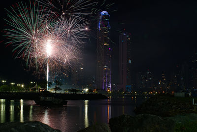 Firework display over river by buildings in city at night