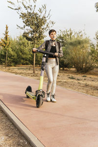 Woman wheeling electric push scooter on footpath