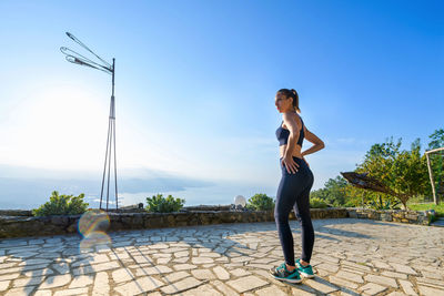 Full length of woman standing on footpath against sky