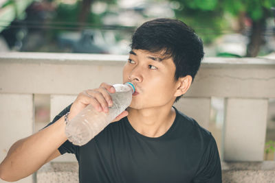 High angle view of young man drinking water while sitting on bench