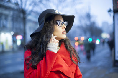 Young woman in warm clothing talking on mobile phone while standing on city street