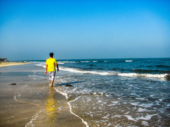 Rear view of man standing on beach against clear sky