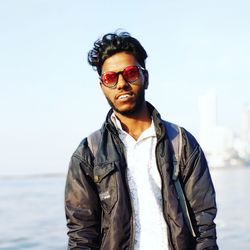 Portrait of young man wearing sunglasses standing against sky