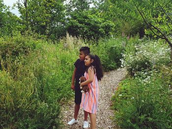 Siblings standing on a pathway looking at the plants in a field of flowers 