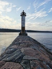 Lighthouse on rock by sea against sky