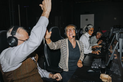 Happy senior couple giving high-five by male and female friends while winning video game at gaming lounge