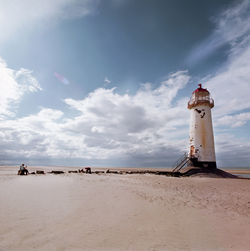 Lighthouse on beach by sea against sky