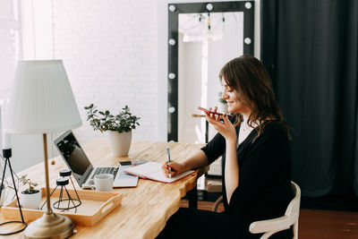 Young woman using phone while sitting on table