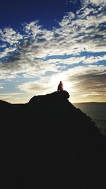 Silhouette people relaxing on rock against sky during sunset