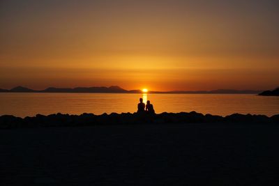 Silhouette of couple sitting on stone at beach