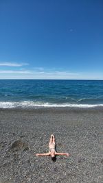 Woman sitting on beach against clear blue sky