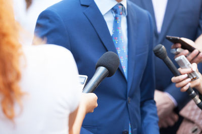 Midsection of interviewer holding microphone against businessman