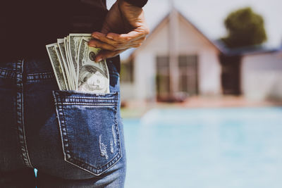 Midsection of man putting paper currency in back pocket