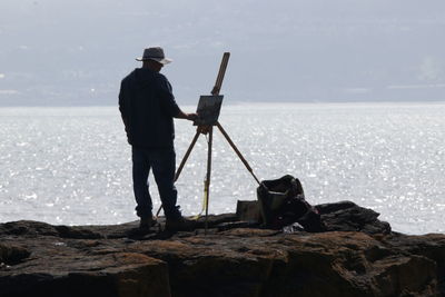 Man standing on rock by sea against sky