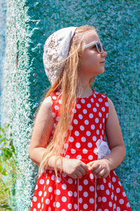 Beautiful happy girl in red polka dot dress smiling turquoise wall background. cute child long hair