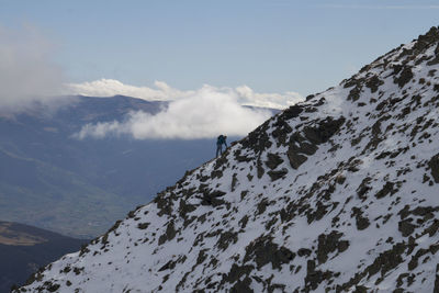 Man climbing on snowcapped mountains against sky