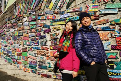 Full length of friends standing against multi colored graffiti