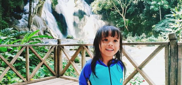 Smiling girl standing by railing against waterfall