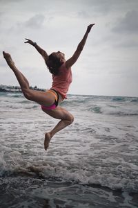 Full length of mid adult woman jumping on beach against sky