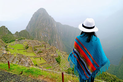 Woman in blue poncho being impressed by the amazing ancient inca citadel of machu picchu, peru