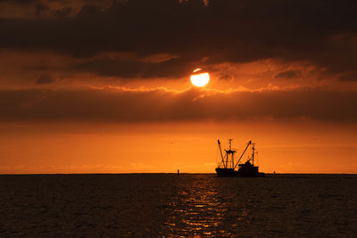 Scenic view of sea against sky during sunset with fishing boat silhouette. 