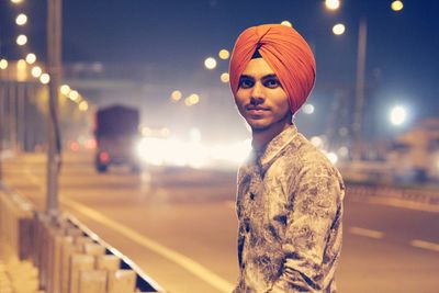 Portrait of teenage boy wearing turban standing on street at night