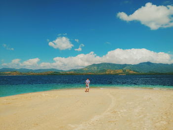 Rear view of man standing on shore at beach against blue sky