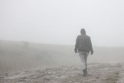 Rear view of woman walking on landscape during foggy weather