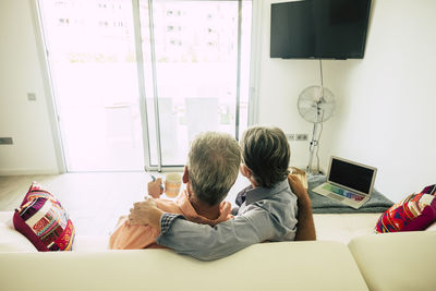 Rear view of senior couple sitting on sofa at home