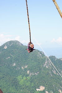 Low angle view of man hanging on rope against sky