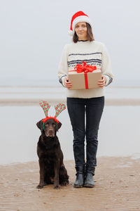 Portrait of young woman with dog standing at beach