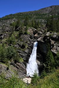 Couple admiring an alpine waterfall in summer, lillaz, aosta, italy