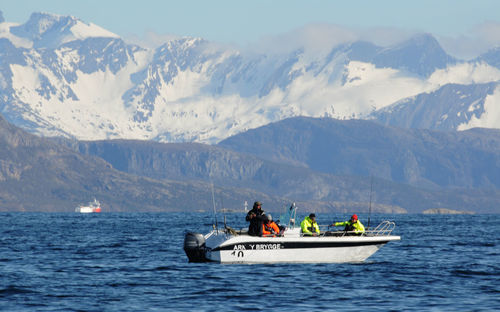 People on boat in sea against mountains