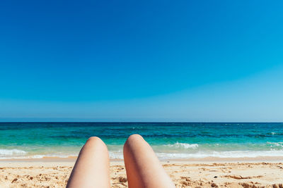 Low section of woman on beach against clear blue sky