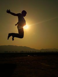 Silhouette man jumping on field against sky during sunset