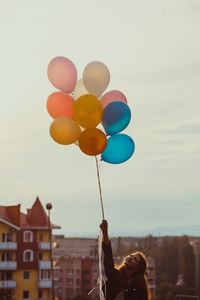 Person holding multi colored balloons against sky