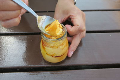 Midsection of person holding pudding in glass on table