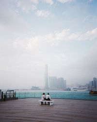 Woman sitting on building by sea against sky