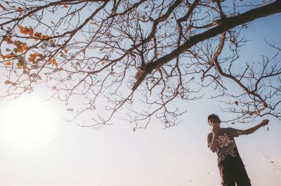 Low angle view of woman standing by tree against sky